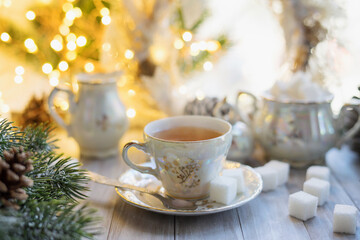 Obraz na płótnie Canvas A cup of English tea from an old mother-of-pearl porcelain service with refined sugar. Christmas tea party breakfast on the background of garlands and fir branches.