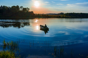 60-year-old Caucasian man with a fishing rod in his hands fishes in a boat with a motor at sunset...