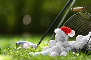 Poster Festive-looking golf ball on tee with Santa Claus' hat on top for holiday season on golf course background.. © amenic181