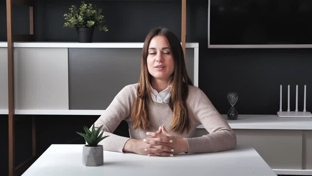 Happy young business woman in beige sweater talks to web camera making distance online video conference call