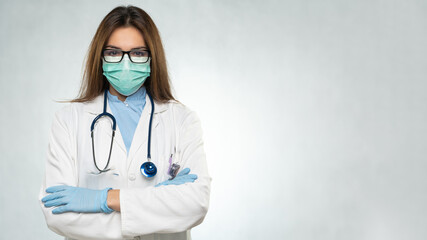 Female young doctor folded hands with protection medical mask, stethoscope over neck and white coat. Covid 19, coronavirus, healthcare concept banner.