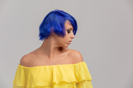 Portrait of a woman with bright colored flying hair, blue haircut. Hair coloring, girl with short hair dressed at yellow dress woth opem shoulders