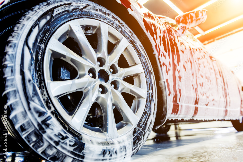 Wall mural Washing red car with active foam at car wash service.