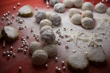 Handmade cookies, decorative snowflakes, decorative pearls and powdered sugar on the table. White on red.