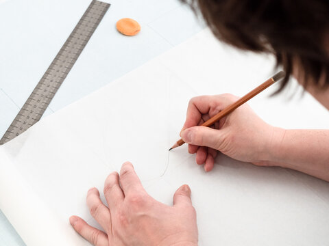 tailor copies pattern layout of dress with pencil and ruler on tracing-paper from graph paper at home