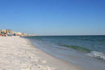 Ocean Coastline with Greenish Water, White Sand Beach, Distant People, and High-Rise Hotels under Clear Blue Sky