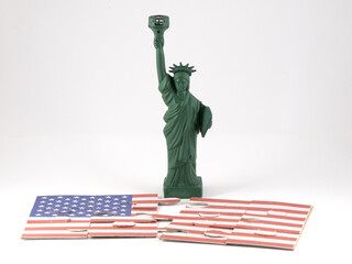 Small replica of the statue of liberty with a puzzle showing the American flag divied at her feet in front of white background