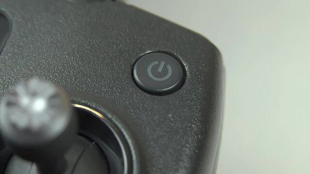 A man's hand presses the power on or off button on the remote control of the drone.