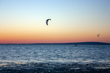 Kitesurfing against the sky at sunset. Riding the waves. Kites in the sky above the sea.