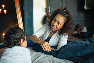 Mother and child bonding in bedroom. Happy caring young mixed race female relaxing at home with her little son, lying together onbed, speaking. Family, relationships and togetherness concept