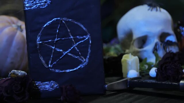 Focus change and smooth camera movement. Close-up of a black book with a pentagram and a human skull. The concept of a witch's table for rituals on the eve of halloween. 