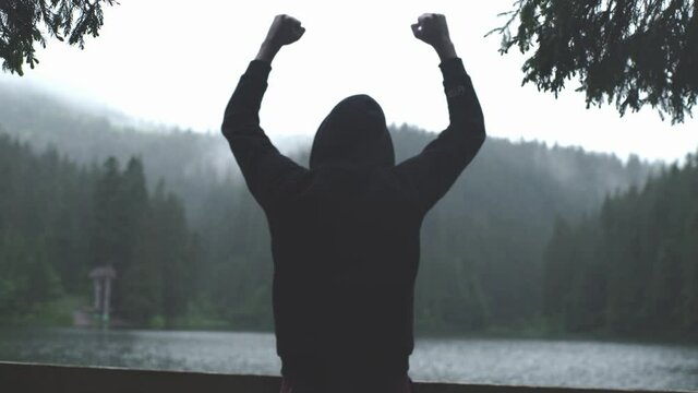 4K back portrait of young attractive bearded man feels happy, positive emotions and success while he standing near nature's miracle mountain alpine lake