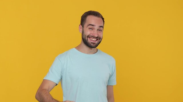 Bearded young man 20s in basic casual blue t-shirt isolated on yellow background studio. People emotions lifestyle concept. Looking at camera waves his hand invites you to go with him come on hurry up