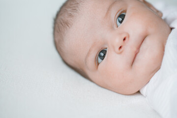 Adorable baby in a white sunny bedroom. Newborn baby is resting in bed. Family morning at home.