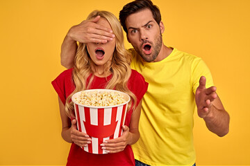 Shocked couple two friends guy girl in 3d glasses isolated on yellow background. People in cinema lifestyle concept. Watching movie film, man closes the girl's eyes during battle scenes in the movie