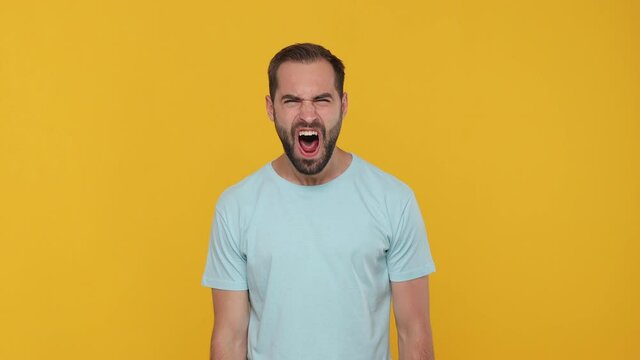 Angry mad crazy swearing bearded young man guy 20s years old in basic casual blue t-shirt isolated on yellow background studio. People sincere emotions lifestyle concept. Looking camera scream shout