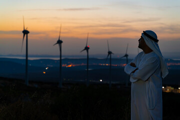 Arab Sheikh with traditional Emirati clothes looking for the energy industry and standing beside a...