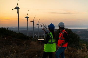Young maintenance engineer team working in wind turbine farm at sunset