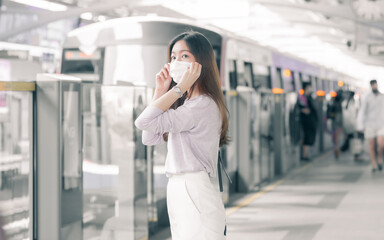 Asian woman wearing mask and standing amonh people at railway station