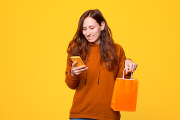 Cheerful young woman is looking and smiling at the phone and is holding a shopping bag .