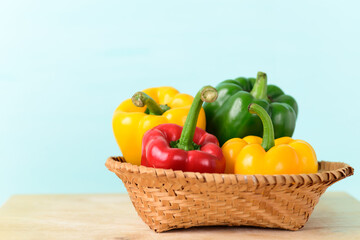 Fresh red, yellow and green bell peppers in a bamboo basket on wooden board with color background, Organic vegetables