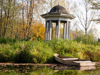 wooden boat on the pond. wooden gazebo on the beach. fallen leaves on the water.