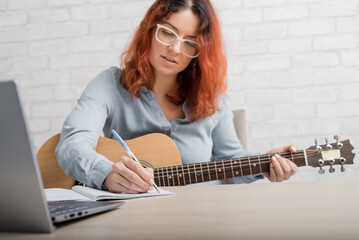 A woman with a guitar writes notes in a notebook. The girl composes a song