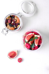 Layered trifle dessert in the glass on the white table. Cherry jam, natural yogurt, granola and raspberry topped with mint. Breakfast idea. Top view