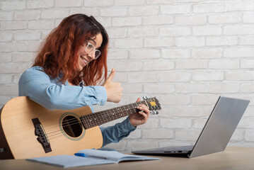 Caucasian woman remotely teaches guitar playing on laptop. Online music training