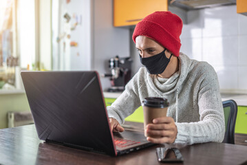 Man in a face mask is using a laptop at home. Concept of remote work, distance communication and lifestyle in a pandemic