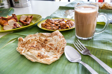 Roti canai or paratha served on banana leaf, with mutton curry and fried chicken, and popular teh tarik