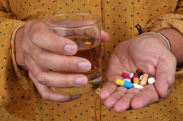Femme avec un mélange de médicaments dans une main et un verre d'alcool dans l'autre en gros plan
