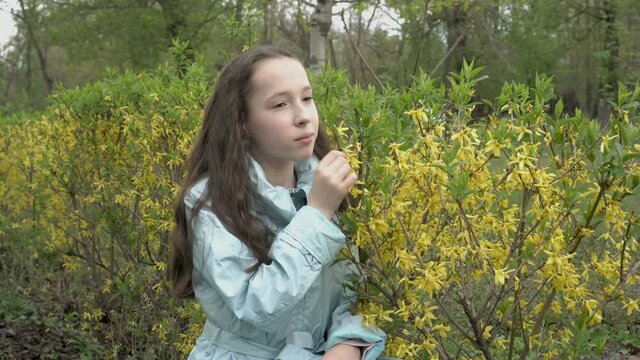 A young teenage girl with long hair sniffs yellow flowers in a city Park and looks thoughtfully at the sky. Female portrait. Close up. Concept. 4K