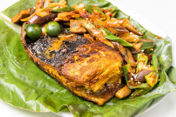 Close-up of popular grilled stingray fish with spices and vegetable served on banana leaf