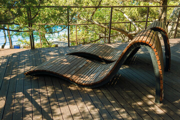 Wooden modern style sunbeds on the flat platform surrounded by growing pine trees near the swimming pool