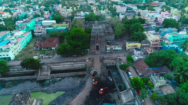 Cleaning the pond near the Hindu temple, the camera moves and passes through the colorful trees and surrounding houses for a top view of the Hindu temple