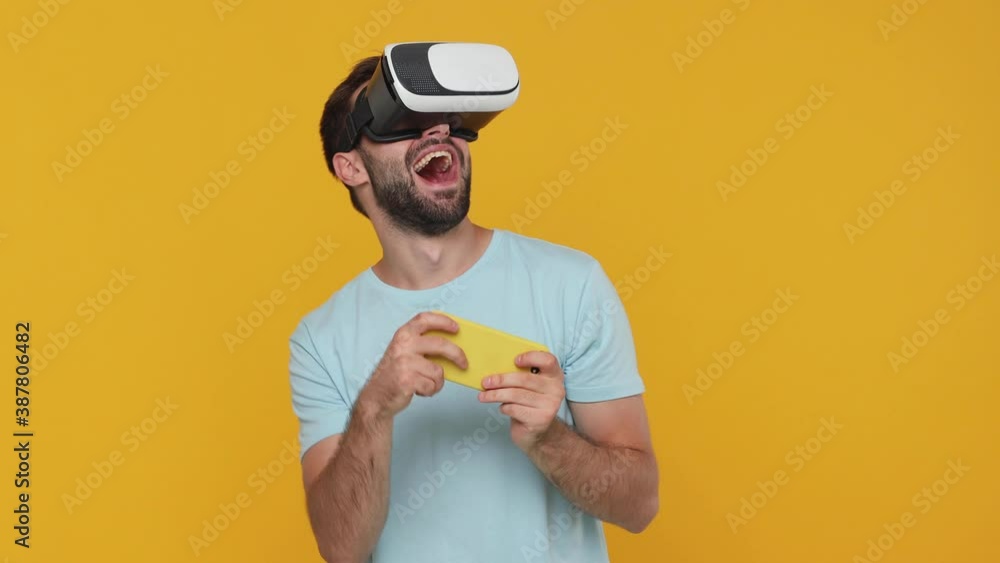 Wall mural gambling young man in blue t-shirt watching vr headset gadget using playing pc race game with mobile