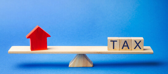 Wooden blocks with the word Tax and a house on scales. The concept of paying taxes on real estate and housing. Debt repayment. Mortgage, loan, credit. Apartment and apartments