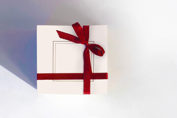 Fototapeta na wymiar Celebration and holiday composition. Christmas, birthday, wedding or anniversary. White gift box on white background, red bow, top view, flat lay. Trendy concept for postcard or invitation