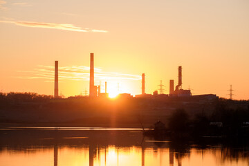 rays of the sun through the factory chimneys during sunset on the shore of the reservoir