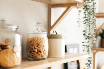 Grocery and kitchenware on the wooden shelves in modern bright kitchen.