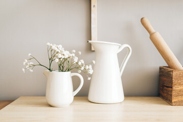 Fototapeta na wymiar White jug and flowers in a vase on a wooden table in the kitchen.