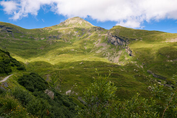 Idyllic landscape with mountain top above green pastures under a blue sky with white clouds high up...