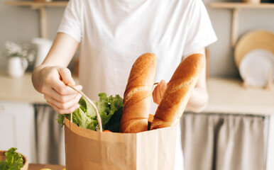 Caucasian woman hold eco shopping bag with fresh vegetables and baguette in modern kitchen.