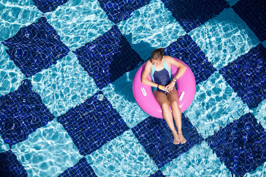 Teen girl floating on pink inflatable ring in hotel swimming pool, top view