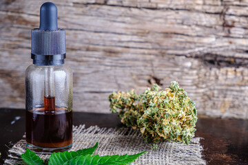 brown medical cannabis resin extract in bottle of medicine dropper. next to marijuana buds and hemp leaf. on hemp sack. Wooden backdround on rust metal suface. horizontal.