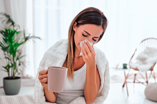 Pretty sick woman has runnning nose, rubs nose with handkerchief, drinks hot beverage, wrapped in warm blanket, has high temperature and cold.