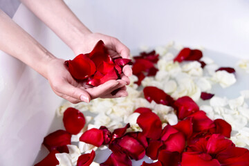 Fototapeta na wymiar girl fill bath with red and white rose petals. concept of cosmetic and salon spa procedures at home