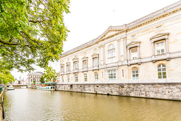 Fototapeta na wymiar The Palace of Justice in Ghent next the Leie River with anchored boats and trees along the river, a relaxed spring day with cloudy sky in Belgium