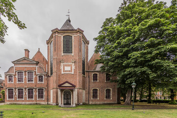 Fototapeta na wymiar Old church with brick walls with multiple windows and crosses on its main tower with a park with lush green trees, cloudy and relaxed day enjoying the city of Ghent, Belgium